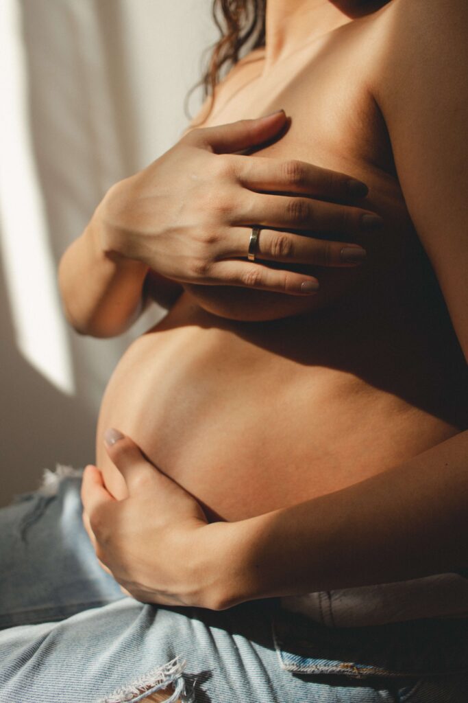 Woman with her hands on pregnant stomach in soft sunlight